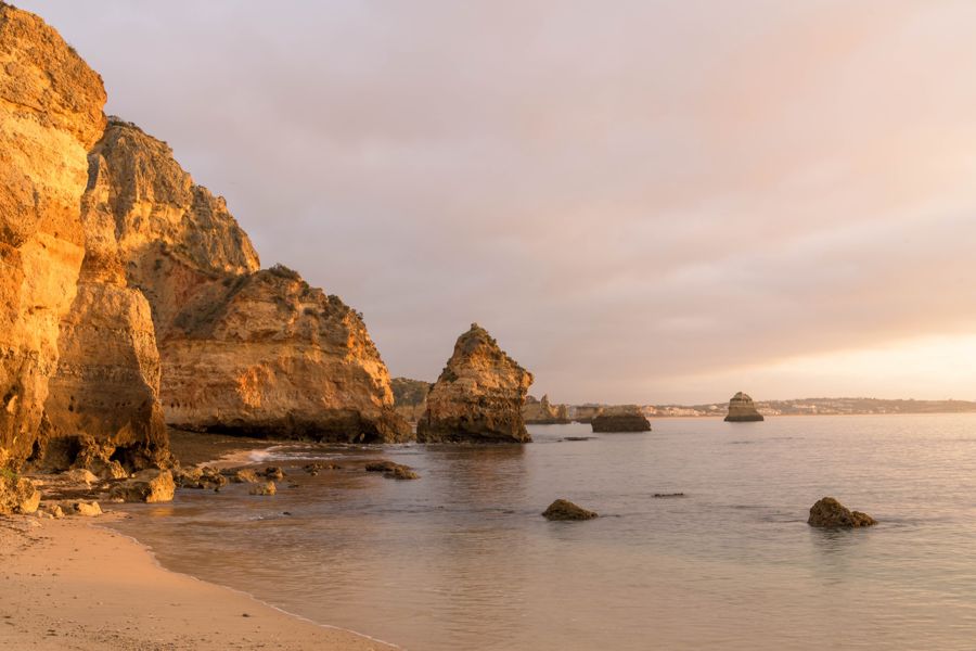 Golden sunrise light on tall sandstone cliffs and sea stacks above a smooth, glassy beach