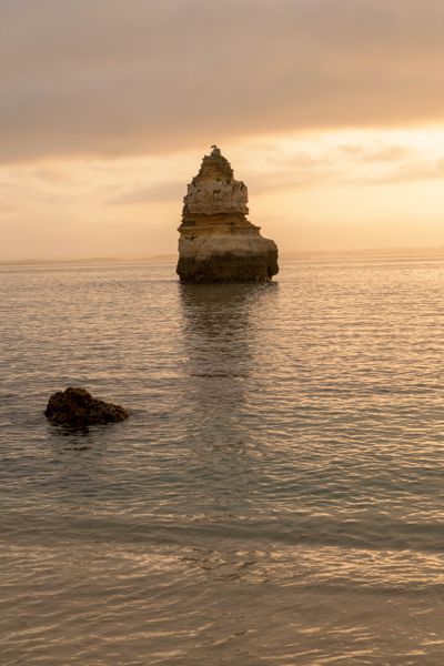 A single pointed sea stack in calm, golden water at sunrise
