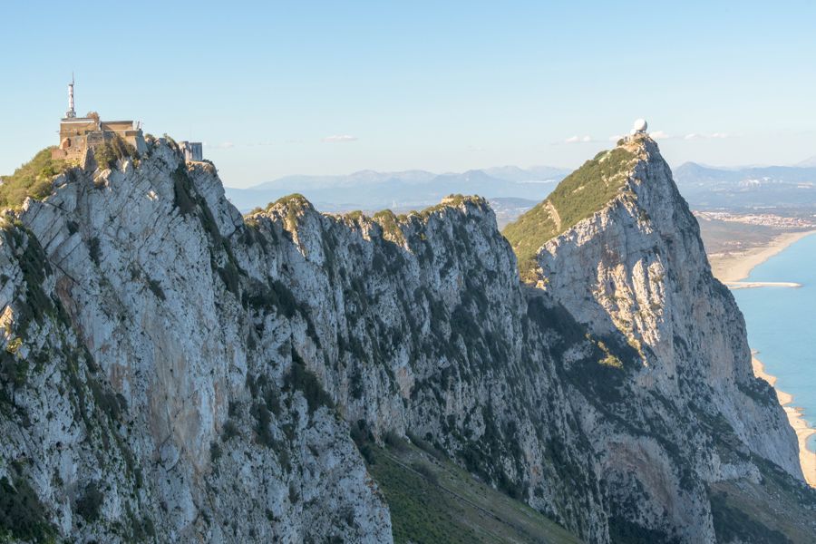 The limestone ridge of the Rock of Gibraltar under a clear blue sky, with a long sandy beach and the sea far below