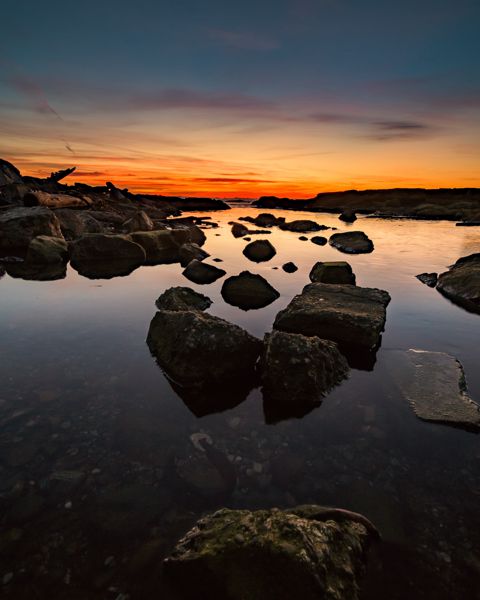 Rocks in a still tide pool reflecting a deep orange band of light after sunset