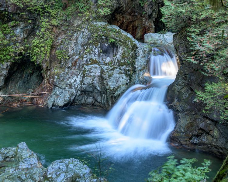 A waterfall stepping down through a mossy granite gorge into a deep emerald-green pool